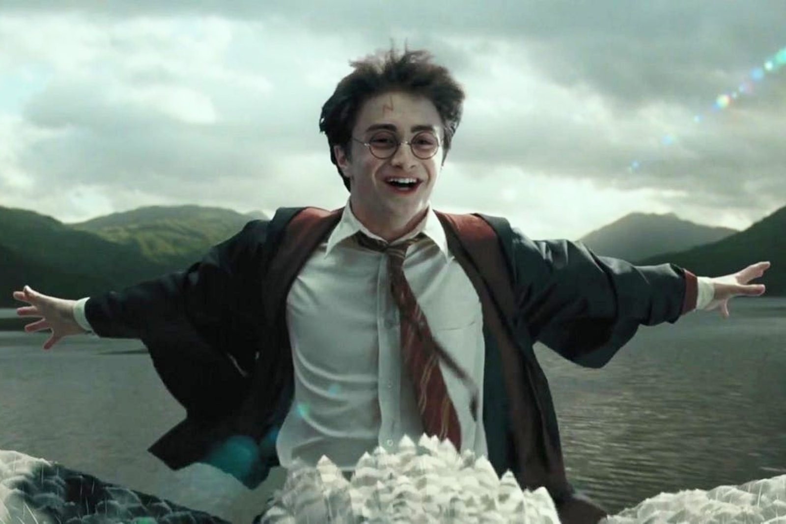 Daniel Radcliffe as Harry Potter, grinning with his arms spread wide as he rides the hippogriff Buckbeak over a lake