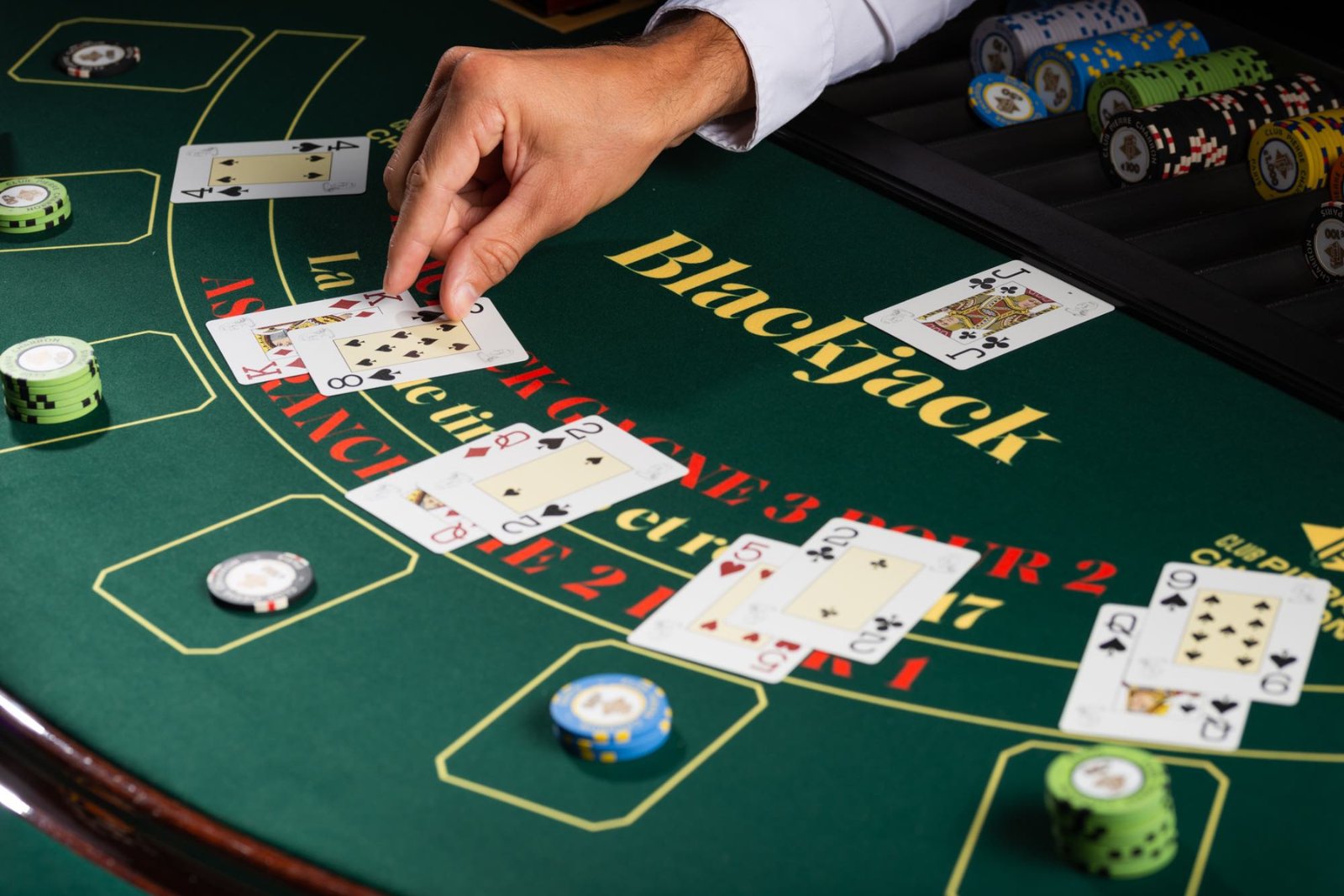 A dealer's hand placing cards on a green blackjack table, with stacks of chips beside the dealt hands