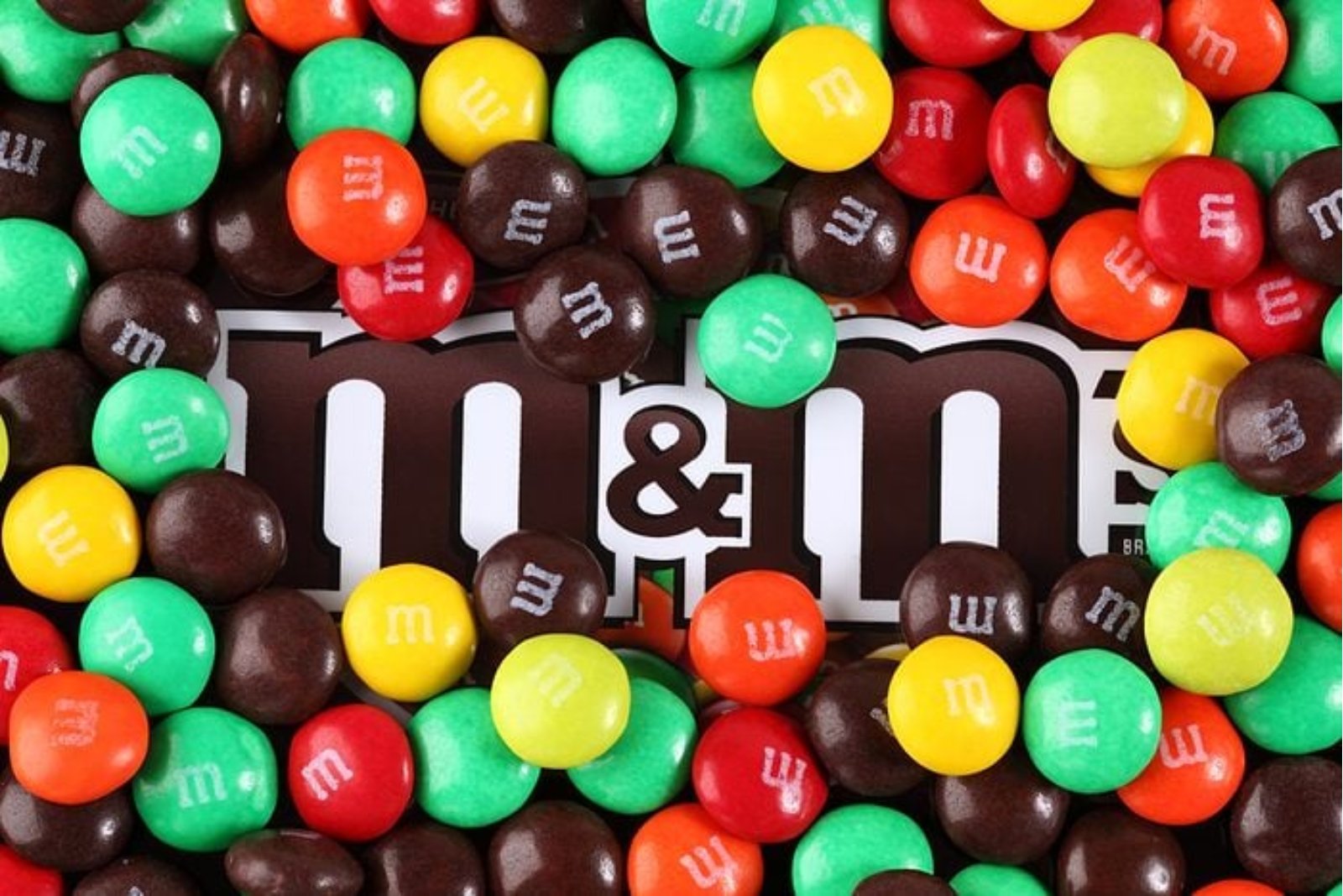 A pile of red, orange, yellow, green and brown M&M's candies scattered over the M&M's logo