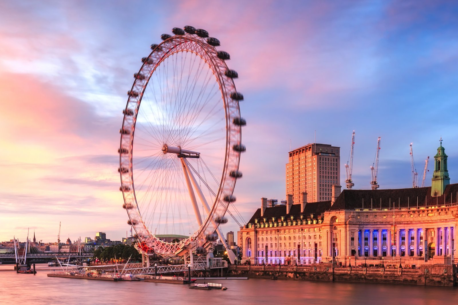 The London Eye beside the River Thames at sunset, its capsules blurred as the wheel turns, with County Hall lit up on the right